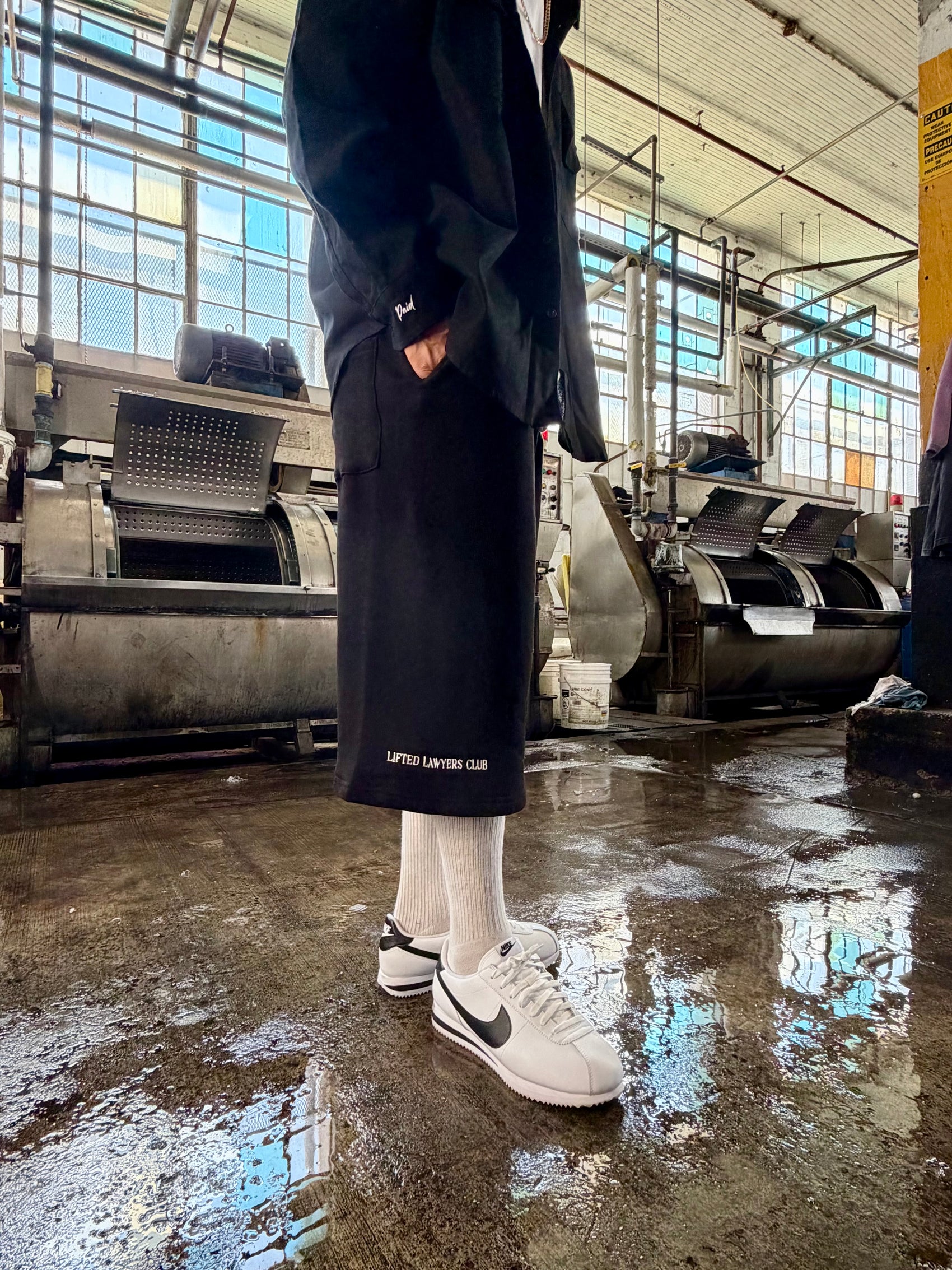 Person wearing a long black coat and white sneakers in an industrial setting
