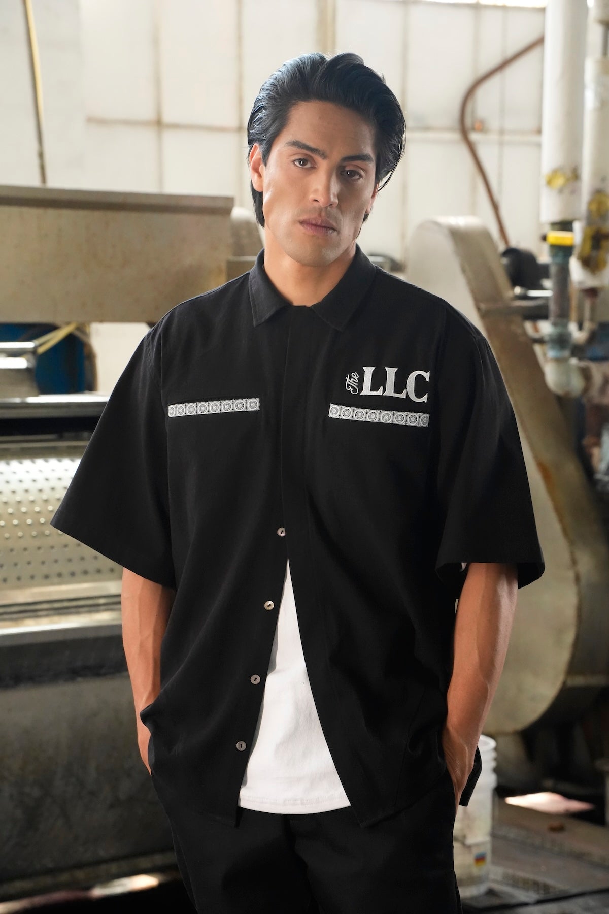 Model wearing the Car Club shirt with 'LLC' logo in an industrial setting (Black)