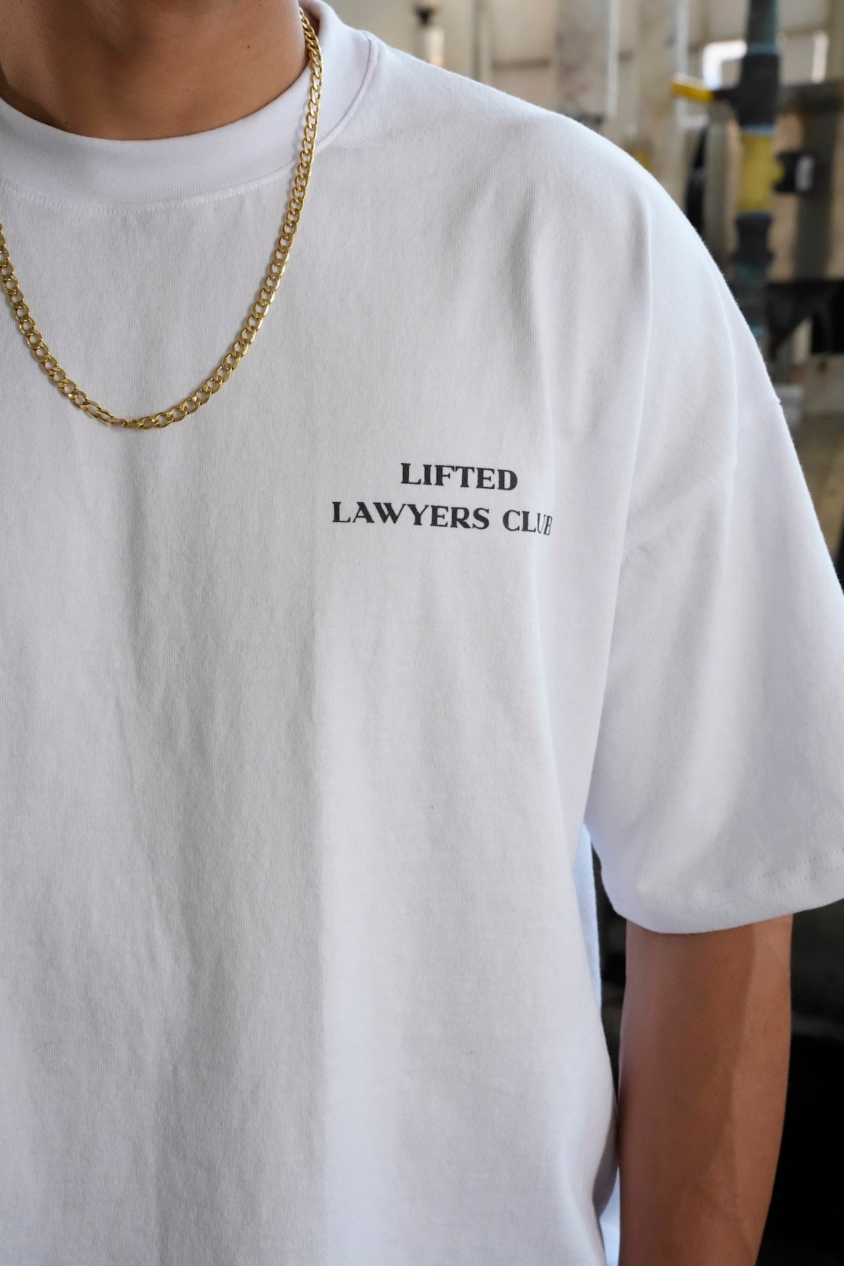 Close-up of Heritage t-shirt with 'Lifted Lawyers Club' text worn by a person, with a gold chain visible (White)