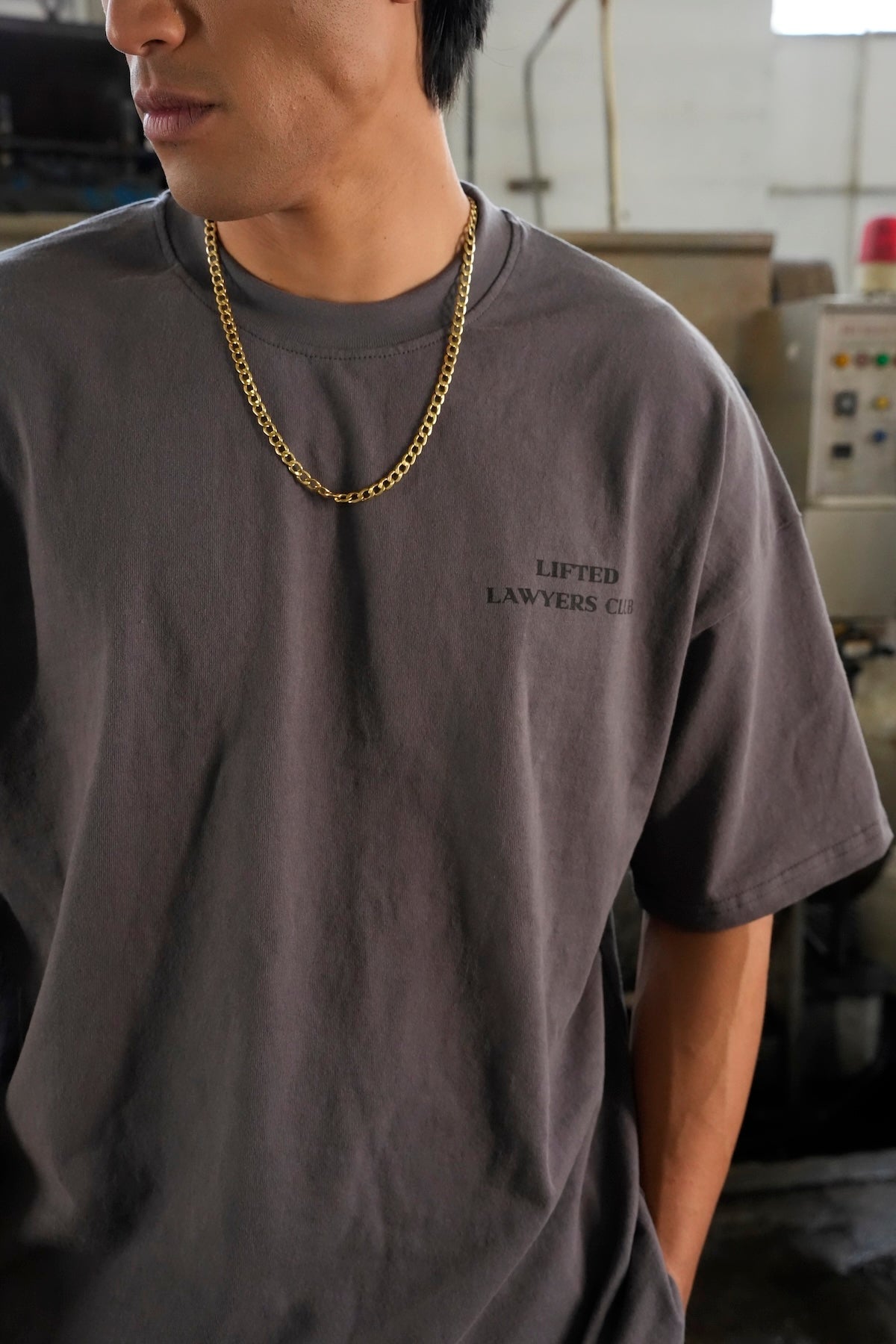 Model wearing a Heritage t-shirt with text and a gold chain necklace in an indoor setting (Gray)